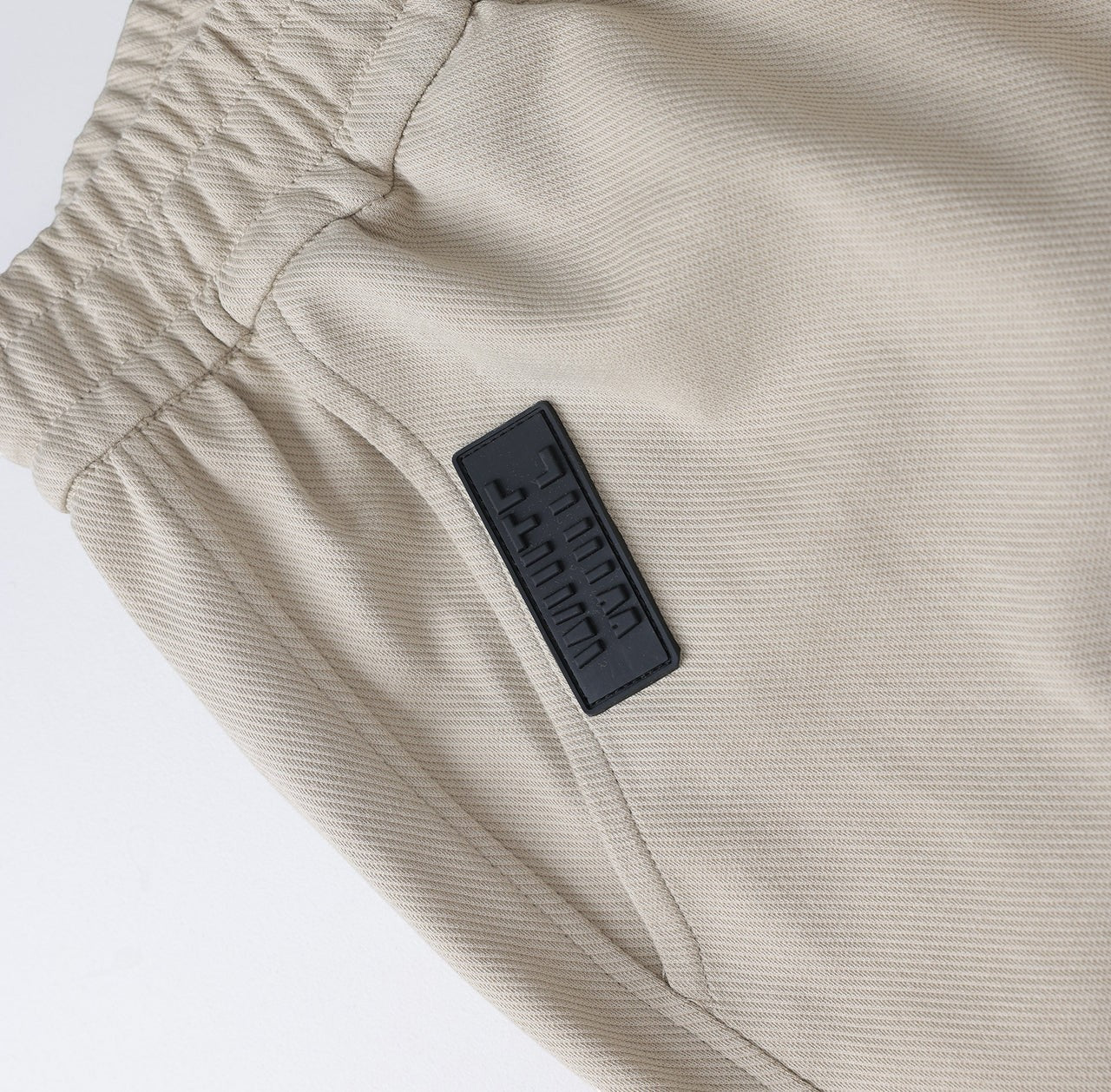 White London Clothing beige casual fit trousers with elastic waistband and black logo patch.
