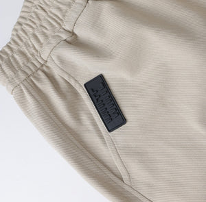White London Clothing beige casual fit trousers with elastic waistband and black logo patch.
