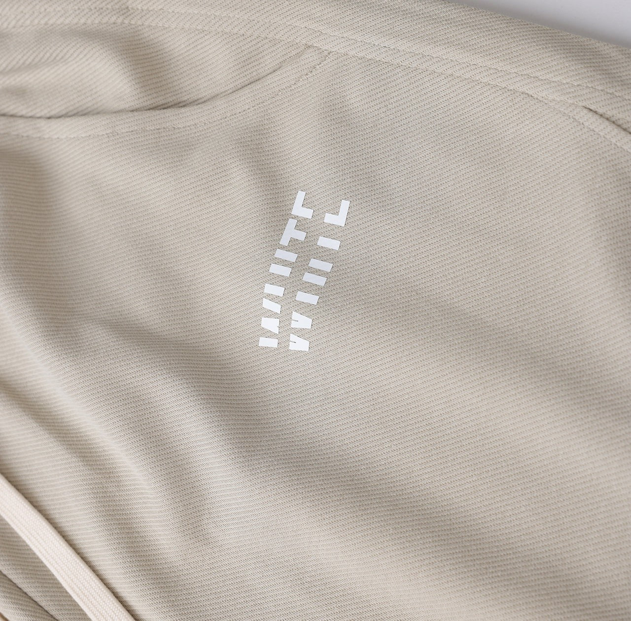 White London Clothing beige relaxed fit trousers with drawstring and white logo detail.