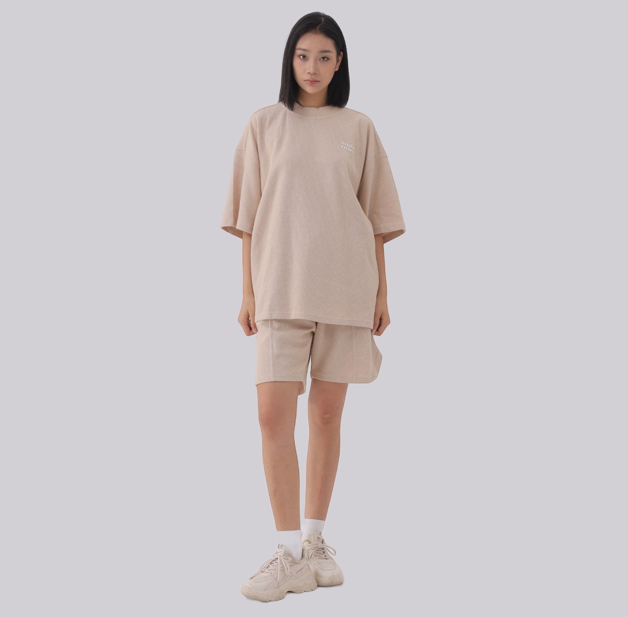 White London Clothing beige oversized textured shorts with elasticated waistband and subtle logo accent on left leg.