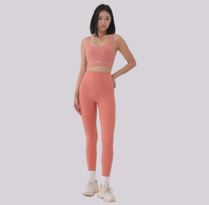 White London Clothing coral pink sculpt sports bra with spaghetti straps and matching leggings. Model wears white socks and sneakers.