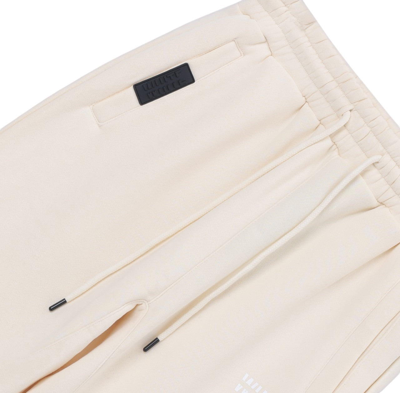 White London Clothing cream cotton jersey joggers with drawstring waist, side pockets, and embossed logo tag on left thigh.