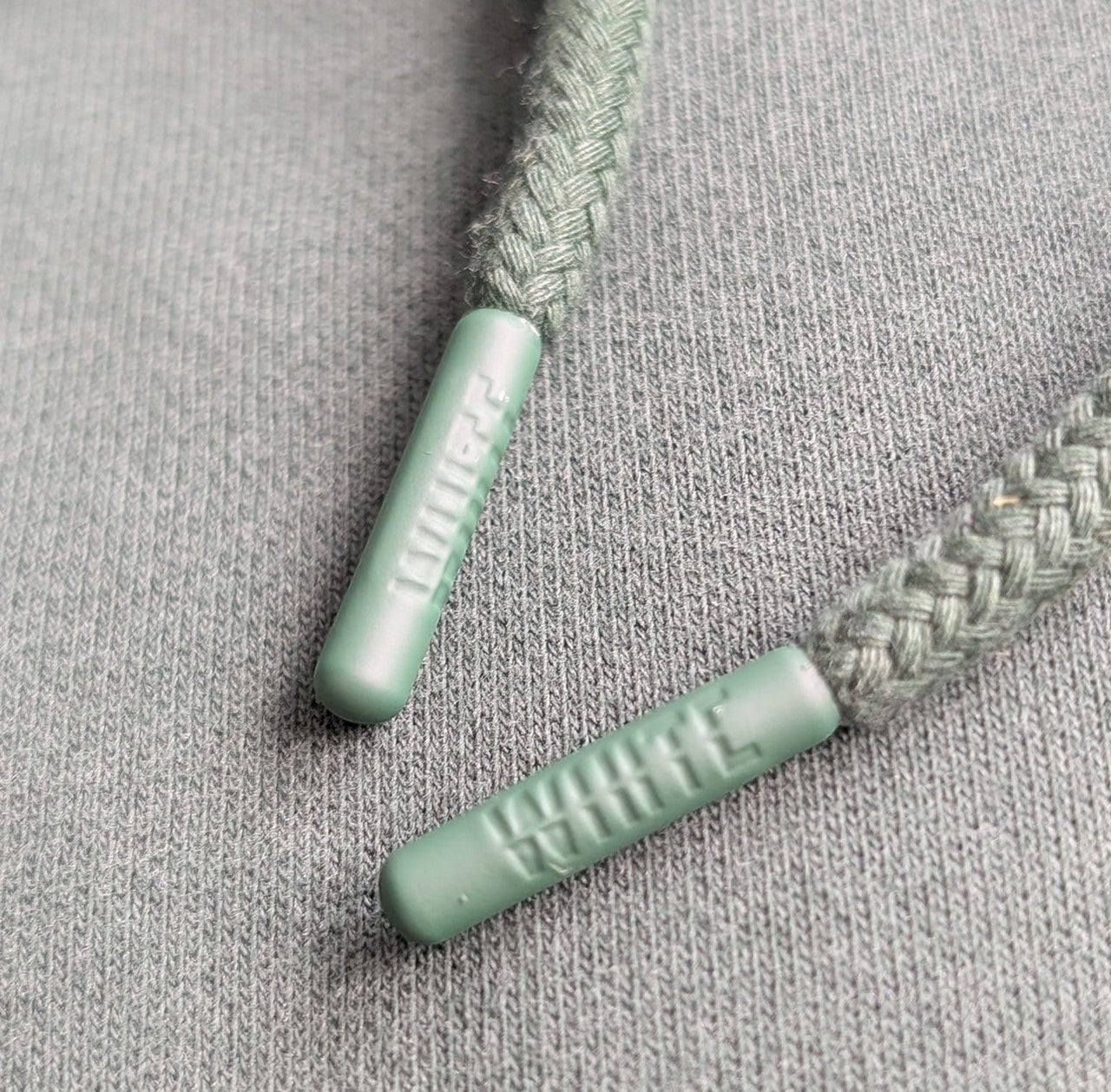 White London Clothing earth green 100% cotton hoodie drawstring tips with embossed logo detail.
